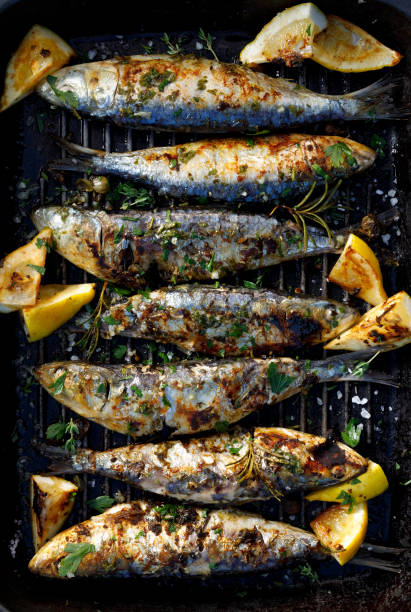 Grilled sardines in a herbal lemon marinade on a grill plate, top view.