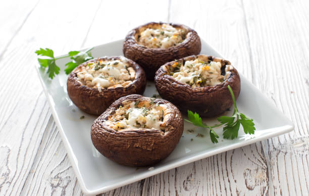 Mushrooms stuffed with cheese and greens Mushrooms stuffed with cheese and greens on white plate  close up stuffed stock pictures, royalty-free photos & images