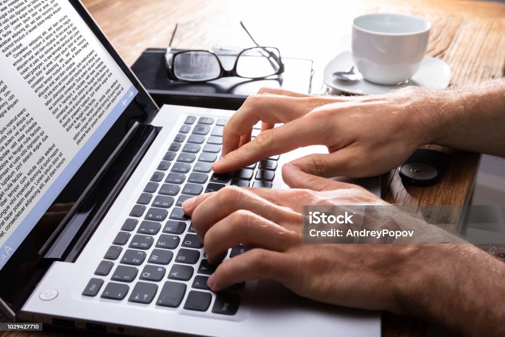 Close-up Of A Person Typing On Laptop Person's Hand Typing On Laptop Over Wooden Desk Writing - Activity Stock Photo