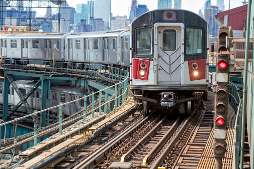 Train approaching  elevated subway station in Queens, New York. Financial buildings and New York skyline are seen in the background, two subway trains speeding one above the other, USA.