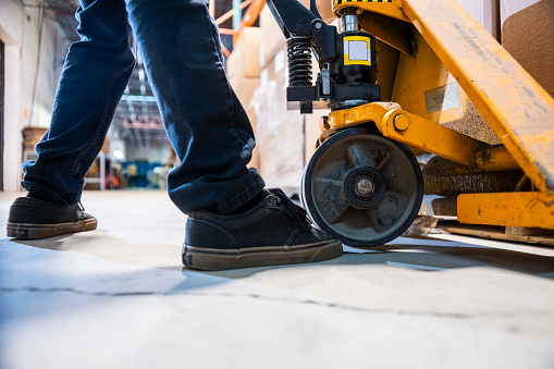 A warehouse worker runs over his toe with a pallet jack. The pallet jack is actually resting on his toe. This is a common injury in industrial warehouses and manufacturing plants.