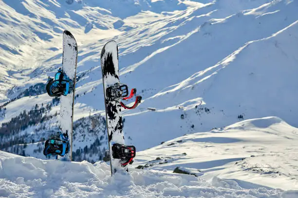 Two snowboard standing upright in snow between mountains on the background