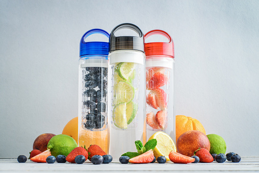 Infused detox water in bottles with fresh fruits and berries on light blue background