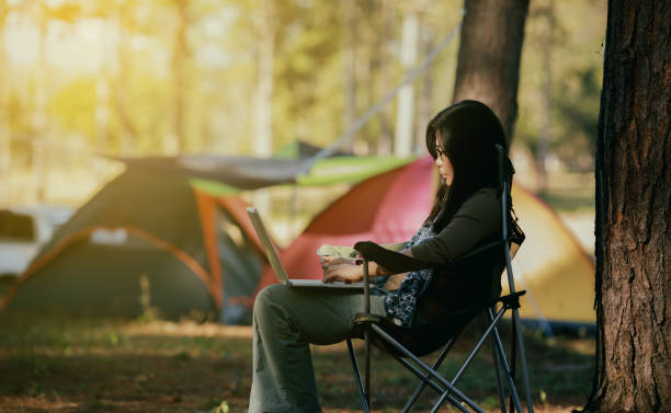 istock Woman Using Laptop While Sitting On Chair Against Trees 1029519110
