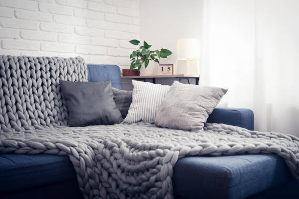 Gray knitted blanket from merino wool Gray knitted blanket from merino wool on couch with pillows in the interior of the living room cozy stock pictures, royalty-free photos & images