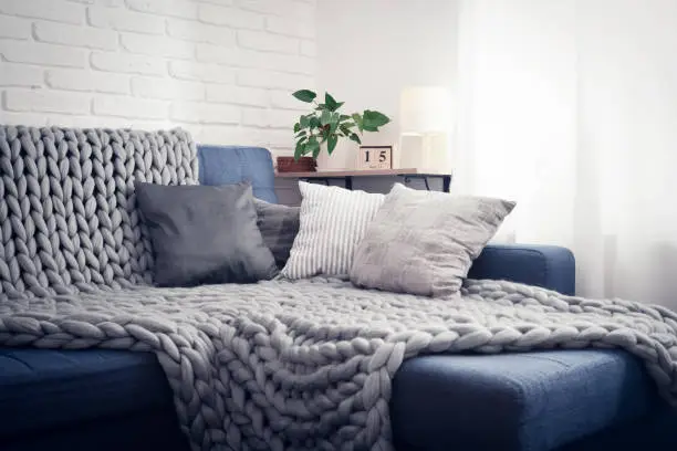 Gray knitted blanket from merino wool on couch with pillows in the interior of the living room