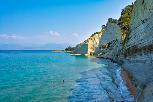 Loggas beach, Peroulades, Corfu island, Greece - August 21 2018: Tourists in Loggas beach which is one of the most special in the island with steep, vertical cliffs which end up on a very narrow, sandy beach.