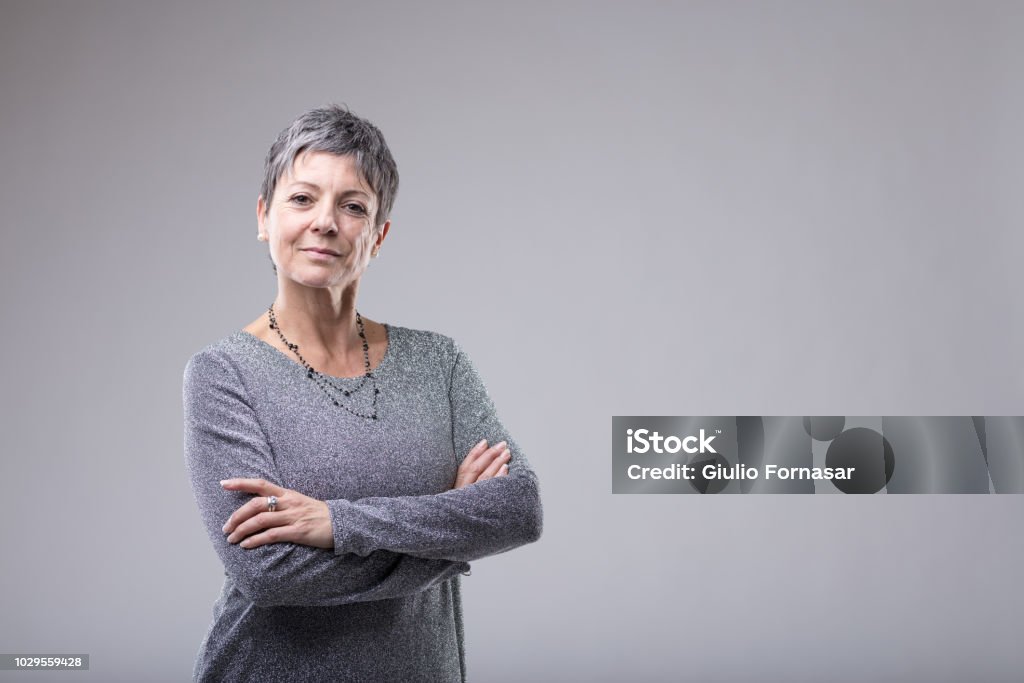 Confident businesswoman with folded arms Confident businesswoman with folded arms standing looking intently at the camera over grey with copy space Women Stock Photo