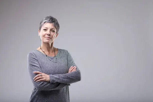 Confident businesswoman with folded arms standing looking intently at the camera over grey with copy space