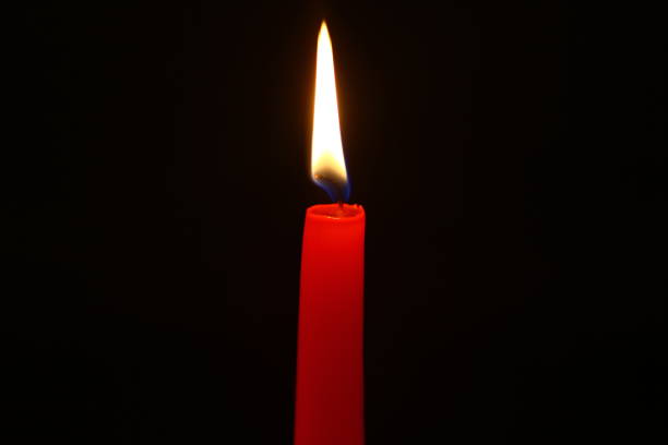 istock cute paraffin lighting red candle with bright flame against heavy black background. 1029630196