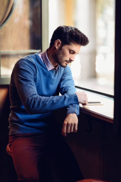 istock Young man with blue sweater looking at his smartphone in a modern pub. 1029678174