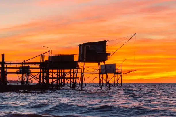 A colouful sunset view of the elaborate walkways on stilts leading to  wooden huts  which are used for fishing using a raditional square net, called a carrelet. that is lowered into the waer and raised again to catch marine life. Located on the Atlantic coast near La Rochell, Charente Maritime, France