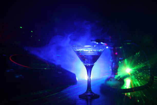 istock Glass with martini with olive inside on dj controller in night club. Dj Console with club drink at music party in nightclub with disco lights. 1029731458