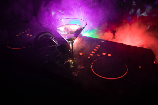 istock Glass with martini with olive inside on dj controller in night club. Dj Console with club drink at music party in nightclub with disco lights. Close up view 1029738382
