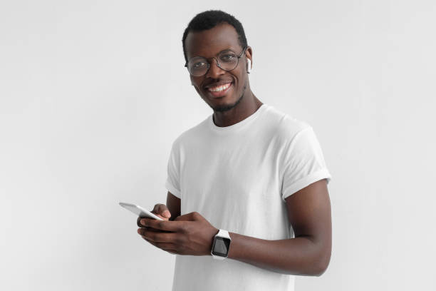 istock Black guy looking and smiling at the camera with cheerful expression while texting his friends, using smartphone, isolated on gray background 1029750774