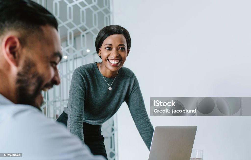 Businesswoman smiling during presentation Businesswoman standing by her laptop and smiling during a board room meeting. Smiling woman giving presentation to her team in conference room. Business Stock Photo