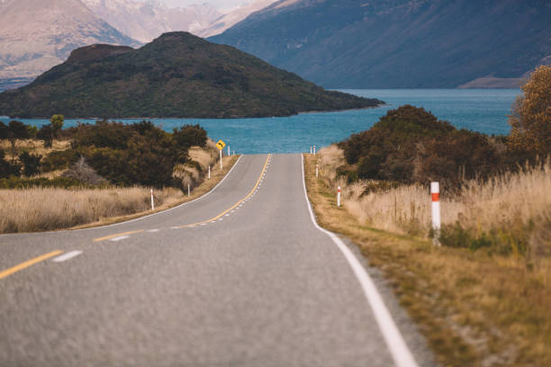 nova zelândia queenstown zona rural estrada caminho para o lago com a montanha como pano de fundo - country road road trip middle of the road south island new zealand - fotografias e filmes do acervo