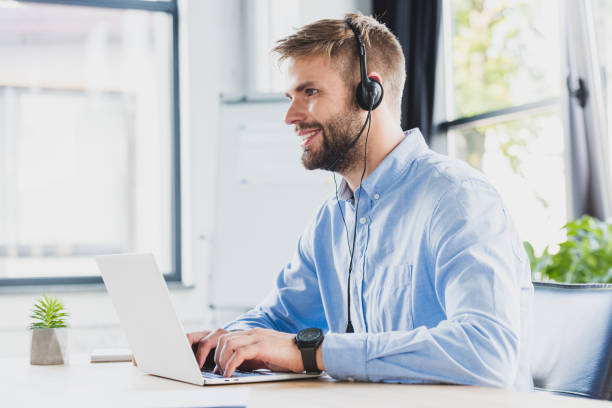 istock side view of smiling young call center operator in headset using laptop in office 1029830790