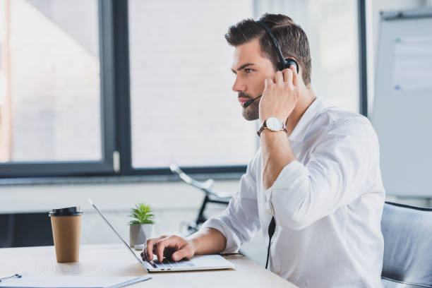 istock side view of young call center operator in headset using laptop and looking away in office 1029830828