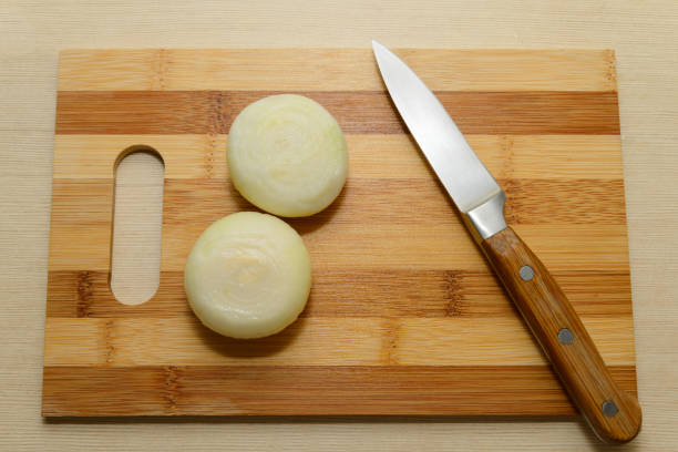 two peeled bulbs and a sharp knife on a wooden board