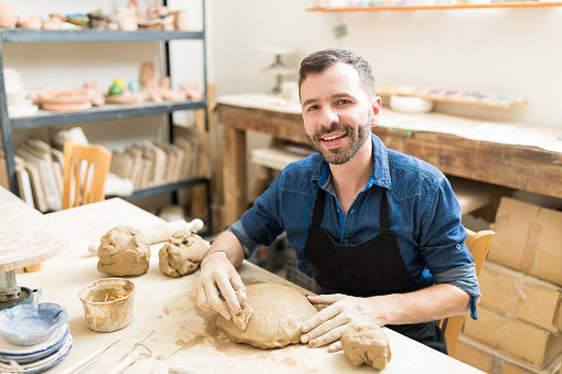 Portrait of confident man shaping clay with sponge in pottery class