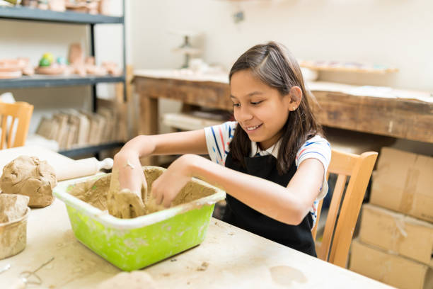 istock Smiling Girl Mixing Clay In Container During Pottery Class 1029864970