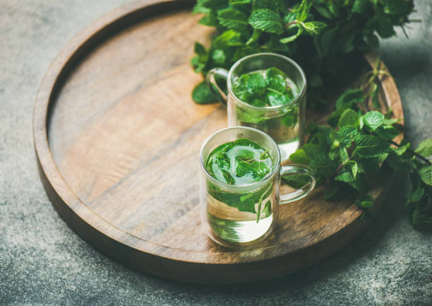 Hot herbal mint tea in glass mugs with leaves Hot herbal mint tea drink in glass mugs with fresh garden mint leaves over wooden tray over concrete background, selective focus, copy space, horizontal composition mint tea stock pictures, royalty-free photos & images