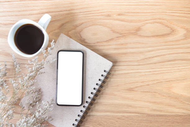 istock Mobile phone with blank screen with book, green leaf, and coffee cup on wooden table background 1029902458