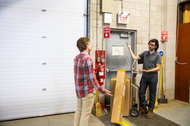 A blocked fire exit door in a warehouse. A supervisor is explaining the dangers of blocking an emergency exit to a new employee.