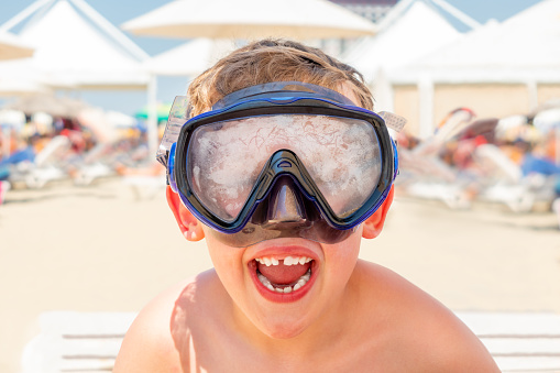 Close-up portrait of a happy laughing boy with diving mask at a sunny beach in Albania Eastern Europe, horizontal composition.