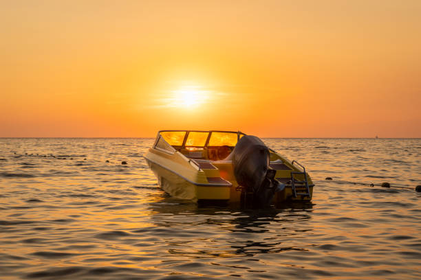 Close beautiful sea view of orange and yellow sunset with a moored motorboat against the horizon. Close beautiful sea view of orange and yellow sunset with a moored motorboat against the horizon. Horizontal composition, taken from shore in Albania Eastern Europe. racing boat photos stock pictures, royalty-free photos & images