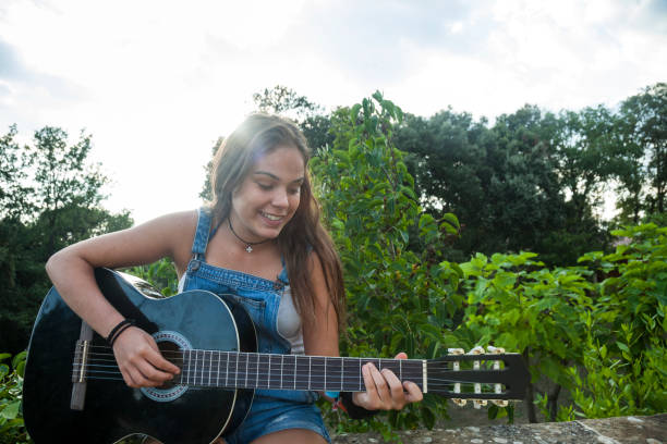 The girl plays the guitar at home. Girl and guitar. High quality photo. The girl plays the guitar and sings songs. Close-up. Playing a stringed instrument.