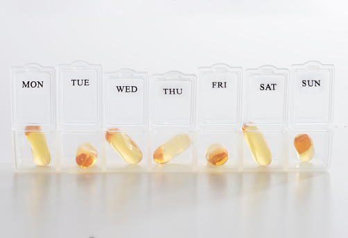 Close up of yellow gel capsules in weekly pill box on white background.