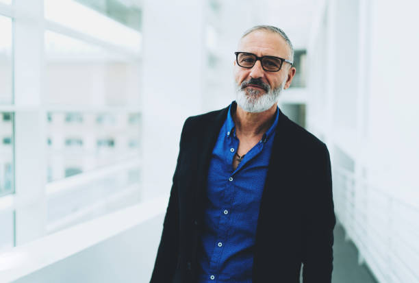istock Successful business coach standing in the office corridor during training session break. University professor looking at the camera while standing in a bright hall with a mobile phone lying on a sill 1029975894