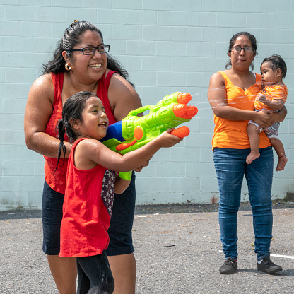 El gran Latino feliz, familia Mexico-Americana - la mujer sonriente optimista positivo de cuerpo, madre, sus hermana y los niños, las niñas de diferentes edades - jugar al aire libre con una pistola de agua y la diversión photo