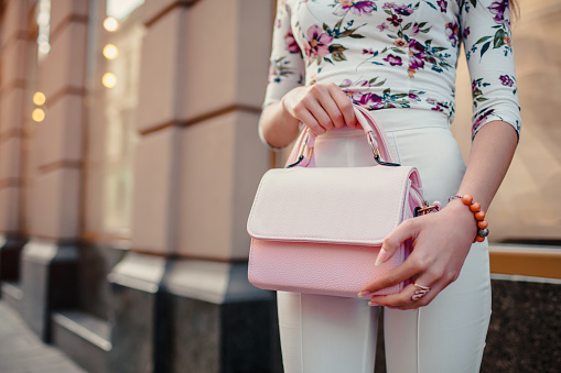 Close-up of stylish female handbag. Young woman wearing beautiful outfit and accessories outdoors on city street.