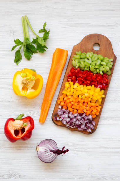 istock Chopped vegetables (carrot, celery, red onion, peppers) arranged on cutting board on white wooden table, high angle view. 1030021834
