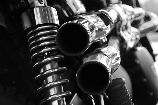 monochrome close up rear view of a powerful classic black vintage motorcycle showing suspension and shiny chrome exhaust pipes