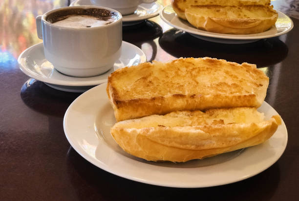 petit déjeuner au brésil avec du pain français grillé avec du beurre sur la plaque avec capuccino sur table. - pao photos et images de collection