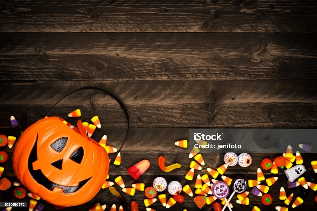 Halloween Jack o Lantern pail with bottom border of spilling candy over dark wood Halloween Jack o Lantern pail with bottom border of spilling candy. Above view on a rustic wood background with copy space. Halloween Stock Photo