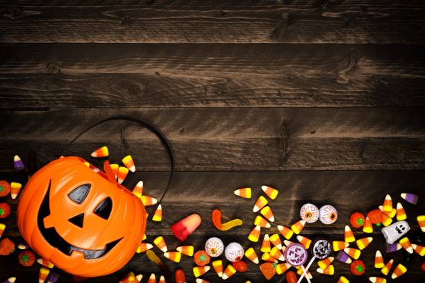 Halloween Jack o Lantern pail with bottom border of spilling candy over dark wood Halloween Jack o Lantern pail with bottom border of spilling candy. Above view on a rustic wood background with copy space. trick or treat photos stock pictures, royalty-free photos & images