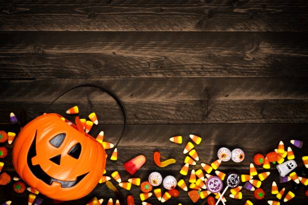 Halloween Jack o Lantern pail with bottom border of spilling candy over dark wood Halloween Jack o Lantern pail with bottom border of spilling candy. Above view on a rustic wood background with copy space. halloween candy stock pictures, royalty-free photos & images