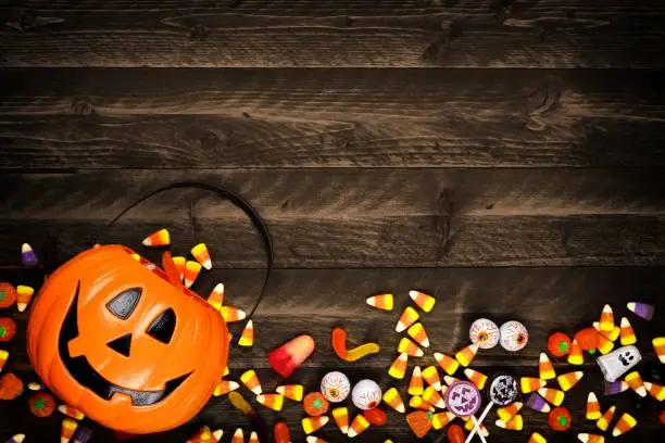 Halloween Jack o Lantern pail with bottom border of spilling candy. Above view on a rustic wood background with copy space.