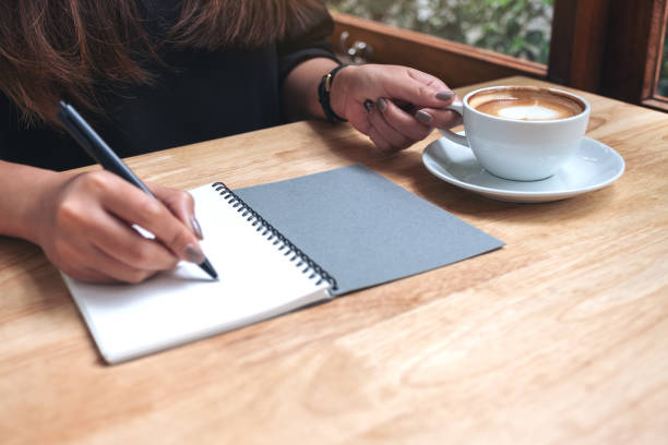 istock Closeup image of a woman's hand writing down on a white blank notebook while drinking coffee on wooden table 1030155098