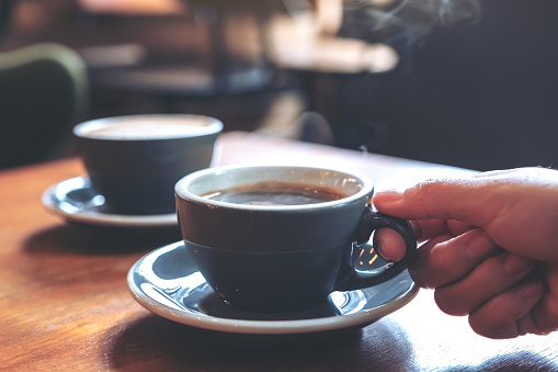 Closeup imagen de una mano sosteniendo una azul taza de café caliente con humo de madera mesa de café photo
