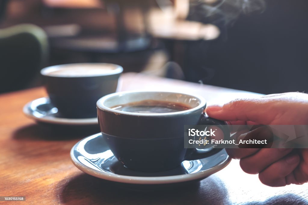 Image gros plan d’une main tenant une tasse bleue de café chaud avec de la fumée sur une table en bois dans le café - Photo de Café - Établissement de restauration libre de droits