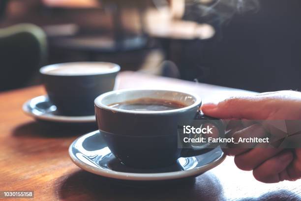 Closeup Image Of A Hand Holding A Blue Cup Of Hot Coffee With Smoke On Wooden Table In Cafe Stock Photo - Download Image Now