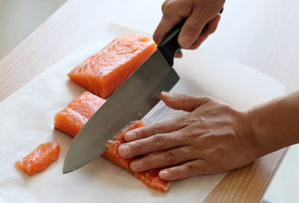istock A hand with a knife cutting raw salmon. 1030157662