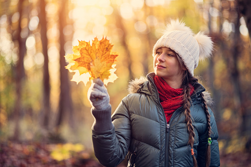Teenage girl enjoying beauty of autumn. They girl is picking up autumn leaves.\nNikon D850