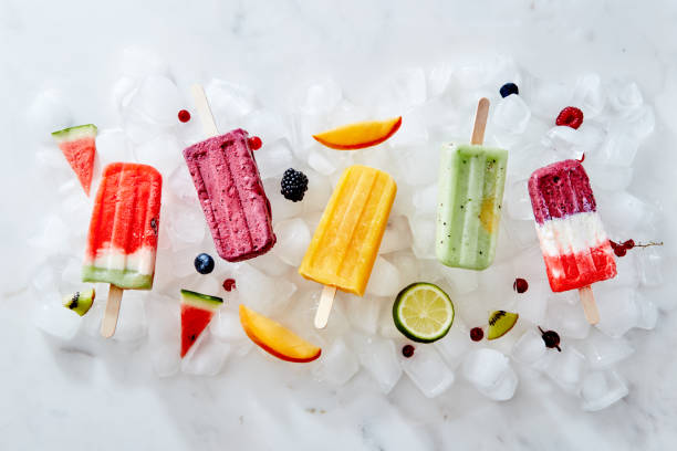 Different ice cream on a stick and different pieces of fruit and berries on ice cubes. Flat lay stock photo